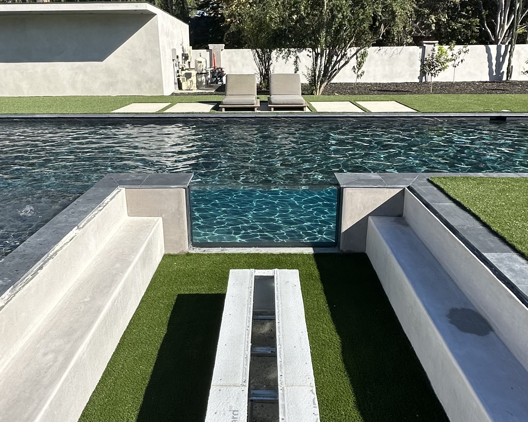 Infinity-edge swimming pool with an acrylic viewing window set into a sunken concrete terrace