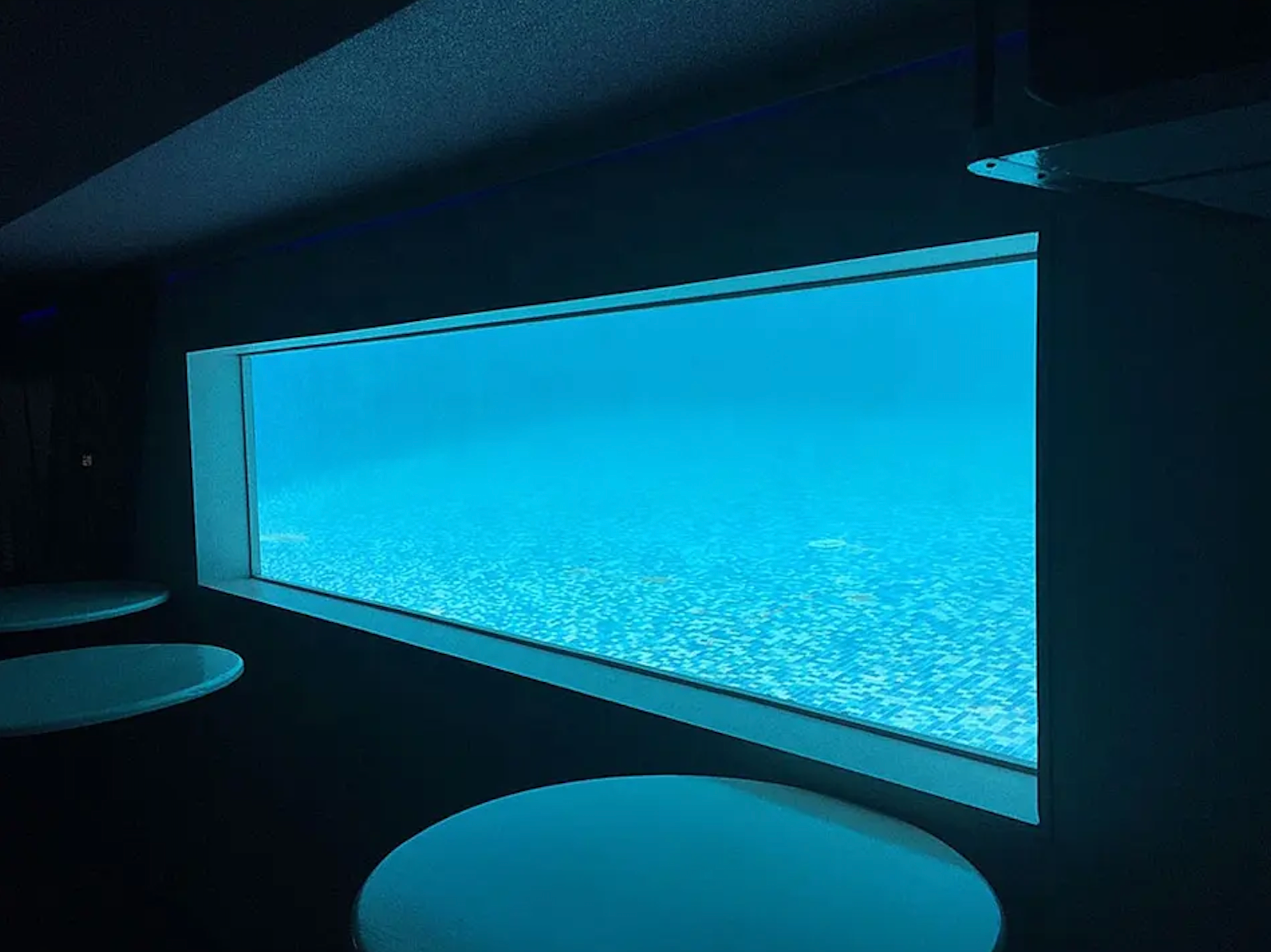 Underwater pool viewing window illuminating an interior lounge