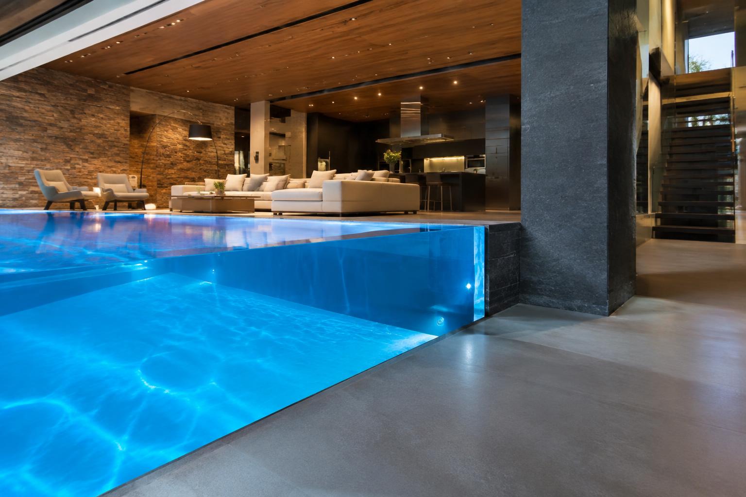 Luxury home interior with a swimming pool acrylic window wall glowing beside the living room