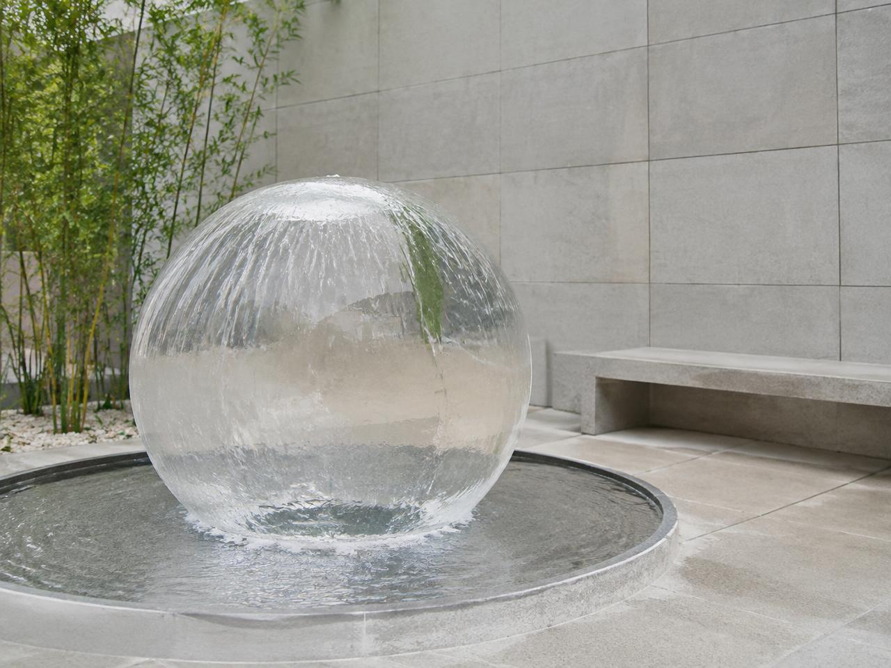 Clear acrylic water sphere with a sheet of water flowing over it in a stone courtyard